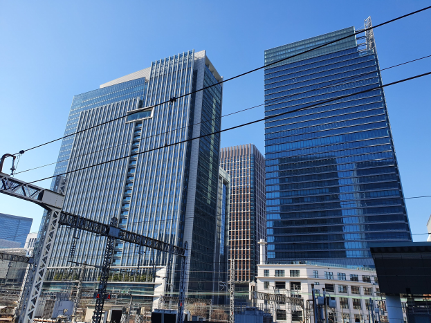 Stadtstraße mit hohen Gebäuden, Strommasten, Drähten, Straßenlaternen, Verkehrszeichen, Bäumen und einem klaren blauen Himmel.