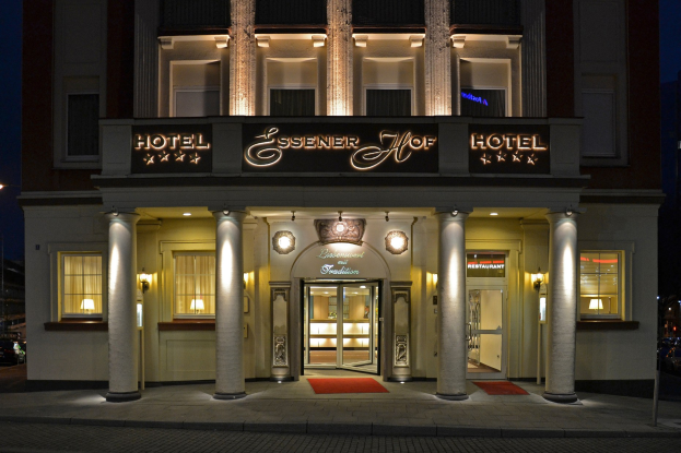 Das Essenerhof Hotel in Berlin, Deutschland, ein mehrstöckiges Gebäude mit Fenstern, Türen, Säulen und einer Namensplakette, mit einer Straße und Fahrzeugen davor und einem klaren Himmel im Hintergrund.