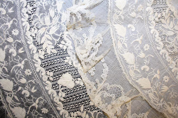 Nahaufnahme eines weißen Hochzeitskleids mit feiner Spitzenverzierung, das feine Muster und einen leichten, luftigen Stoff zeigt.