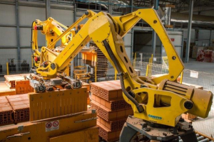 Großes industrielles Lager mit gestapelten Kisten, Kränen, Zaun, Pfählen und einer fernen Wand in einer automatisierten Fertigungsumgebung.