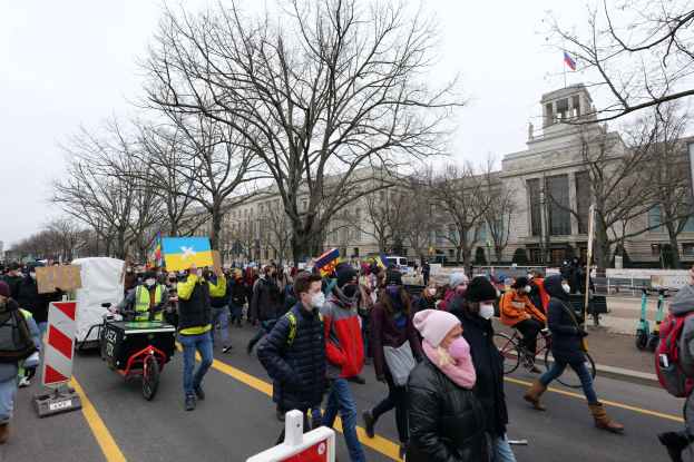 Eine große Gruppe von Menschen nimmt an einer Protestdemo in Washington, D.C. am 21. Januar 2020 teil und marschiert eine Straße entlang mit Plakaten, Bannern und Fahrrädern vor einem Gebäude und einem klaren blauen Himmel.