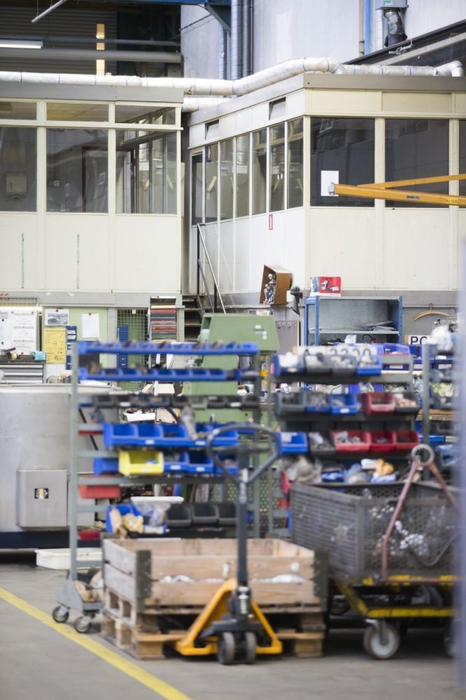 Ein großes Lager, das mit verschiedenen Geräten wie Wagen, Schränken und einer Box gefüllt ist, mit einer Glaswand und Rohren im Hintergrund.