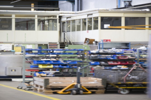 Ein großes Lager, das mit verschiedenen Geräten wie Wagen, Schränken und einer Box gefüllt ist, mit einer Glaswand und Rohren im Hintergrund.