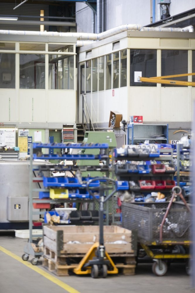 Ein großes Lager, das mit verschiedenen Geräten wie Wagen, Schränken und einer Box gefüllt ist, mit einer Glaswand und Rohren im Hintergrund.