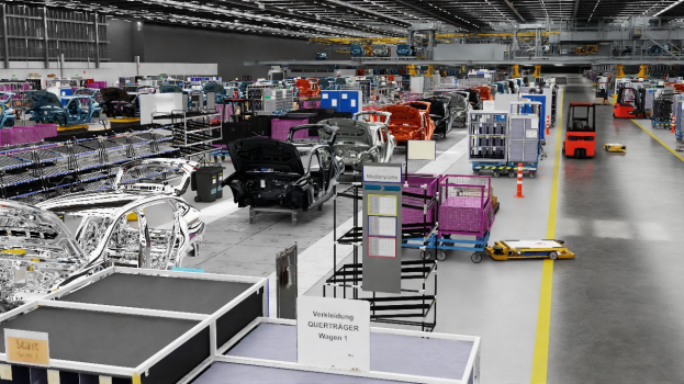 Eine große Volkswagen-Fabrik-Montageband mit zahlreichen Autos in verschiedenen Produktionsstadien, metallischen Strukturen links und rechts, ein paar Fahrzeuge auf dem Boden, eine Wand im Hintergrund und an der Decke angebrachte Leuchten.